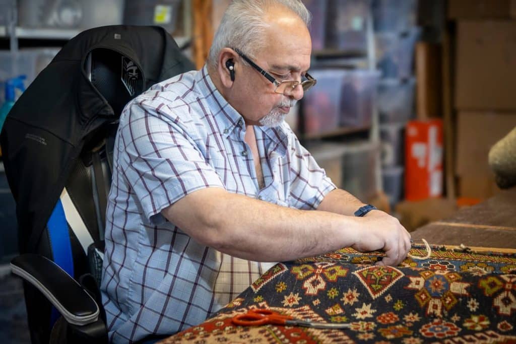 Master Persian carpet weaver restoring a handmade rug at Shenasi Carpet in Vancouver