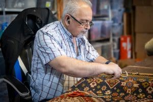 Master Persian carpet weaver restoring a handmade rug at Shenasi Carpet in Vancouver