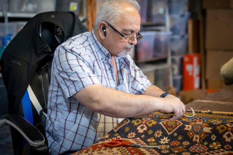 Master Persian carpet weaver restoring a handmade rug at Shenasi Carpet in Vancouver
