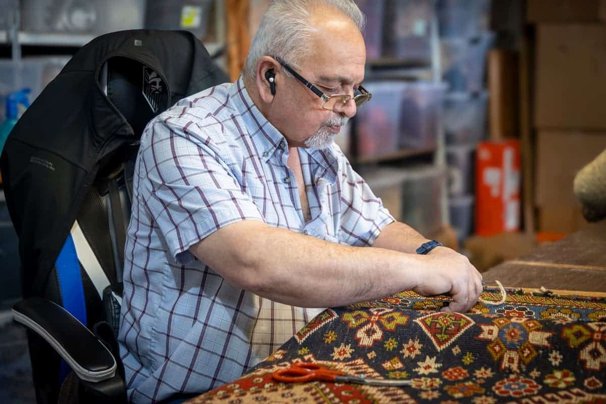 Master Persian carpet weaver restoring a handmade rug at Shenasi Carpet in Vancouver