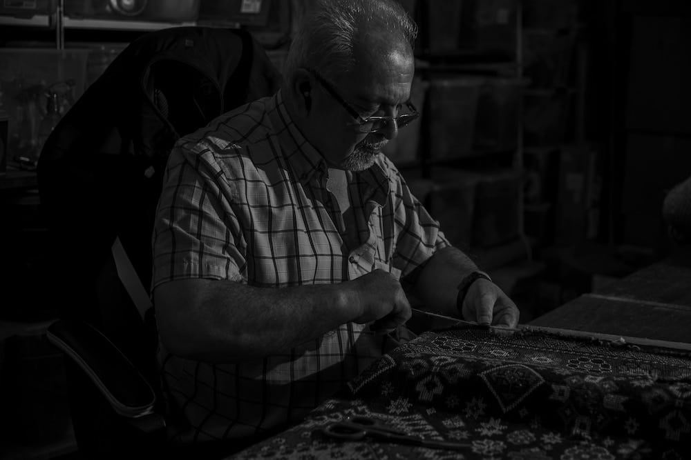 Master rug repair artisan restoring a Persian carpet at Shenasi’s Vancouver workshop