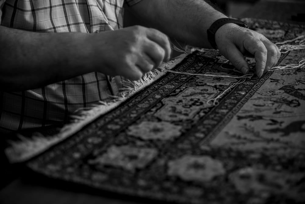 Hands of a skilled craftsman performing fringe repair on a Persian carpet in Vancouver