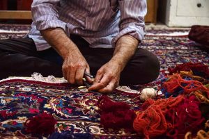 A skilled artisan repairing a Persian carpet by hand with traditional tools and wool threads.